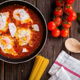 Black Frying Pan With Spaghetti Sauce Near Brown Wooden Ladle and Ripe Tomatoes